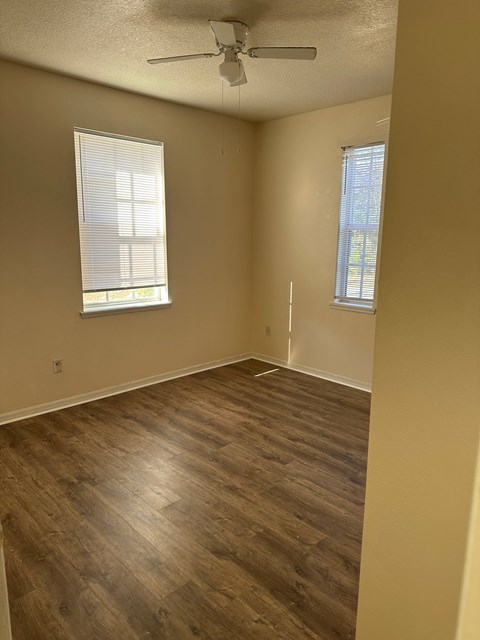 A room with a ceiling fan and two windows.