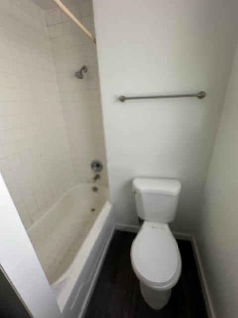 A white toilet in a small bathroom with a white tiled shower.