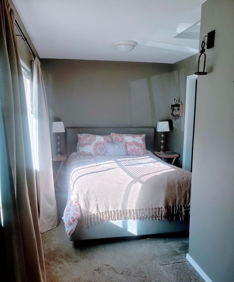 A bedroom with a bed, two lamps, and a nightstand.