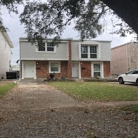 A white car is parked in front of a brick house.