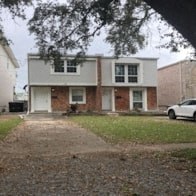 A white car is parked in front of a brick house.