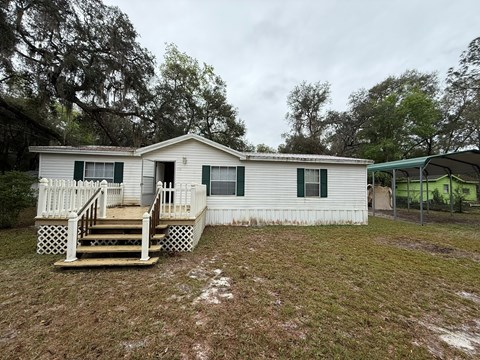 A white house with a green awning and a wooden deck.