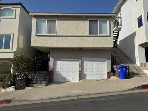 A two-story beige house with a white garage door and a blue trash bin outside.