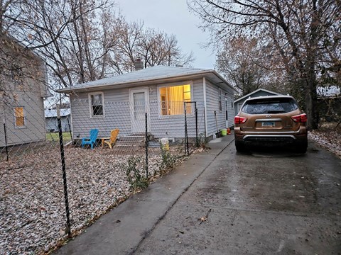 A brown car is parked in front of a grey house.