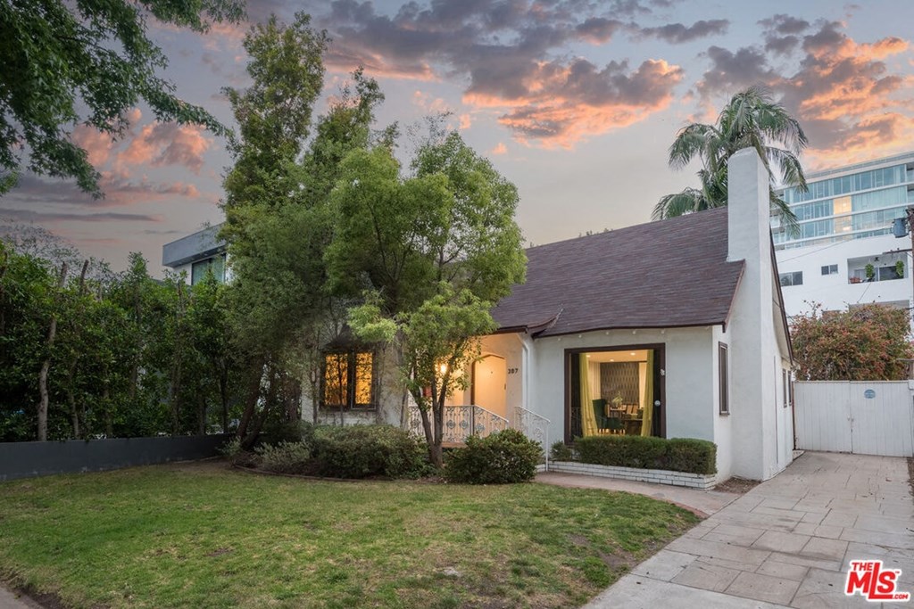 A white house with a brown roof and a tree in front of it.