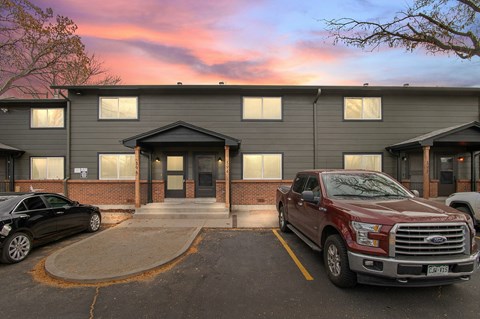 A red truck is parked in front of a building with a black car to its left.