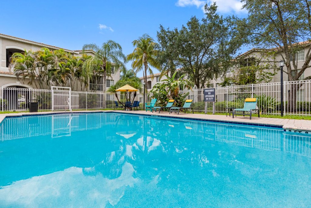 A person is swimming in a pool with a fence and trees in the background.