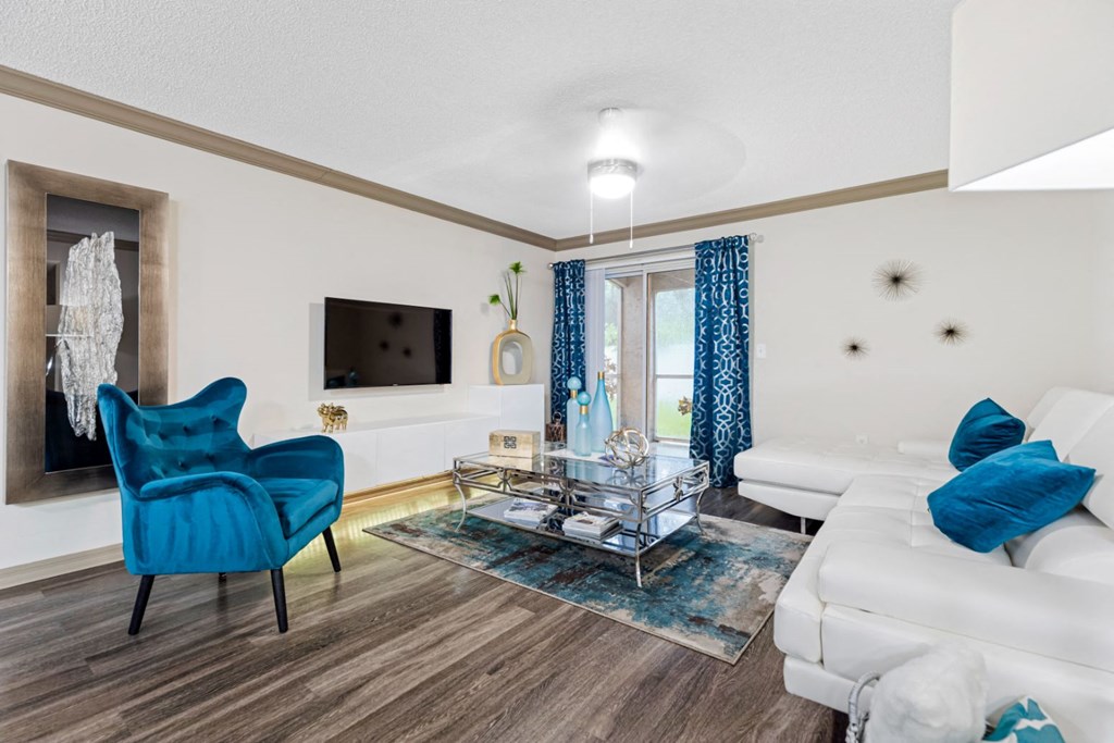A blue chair sits in a living room with a white couch and a glass coffee table.