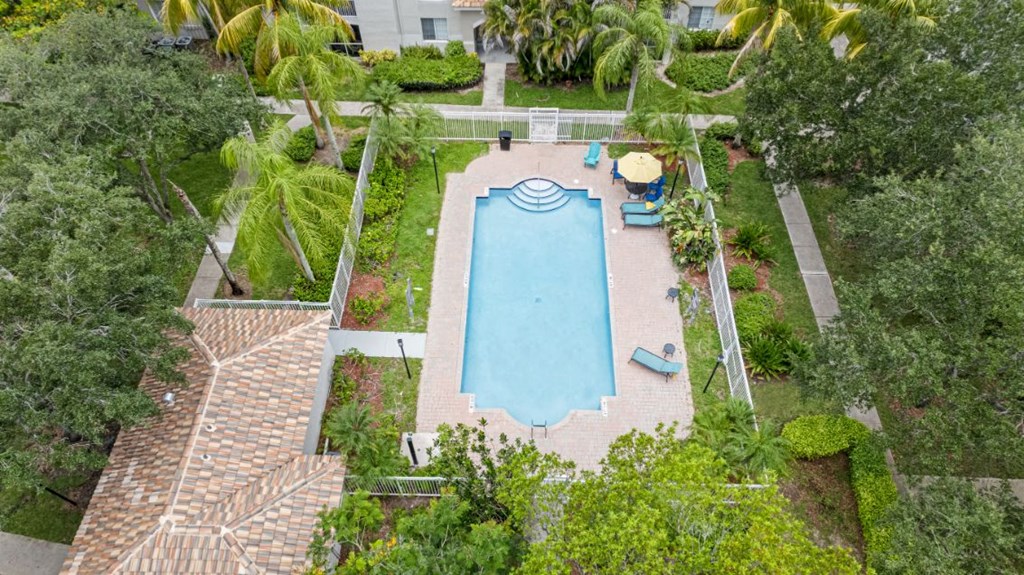 A swimming pool surrounded by greenery and a white fence.