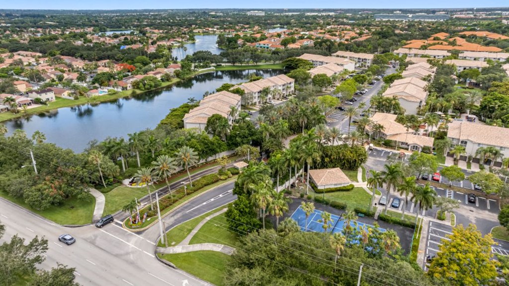 A view of a residential area with a road, a car, a swimming pool, and a body of water.