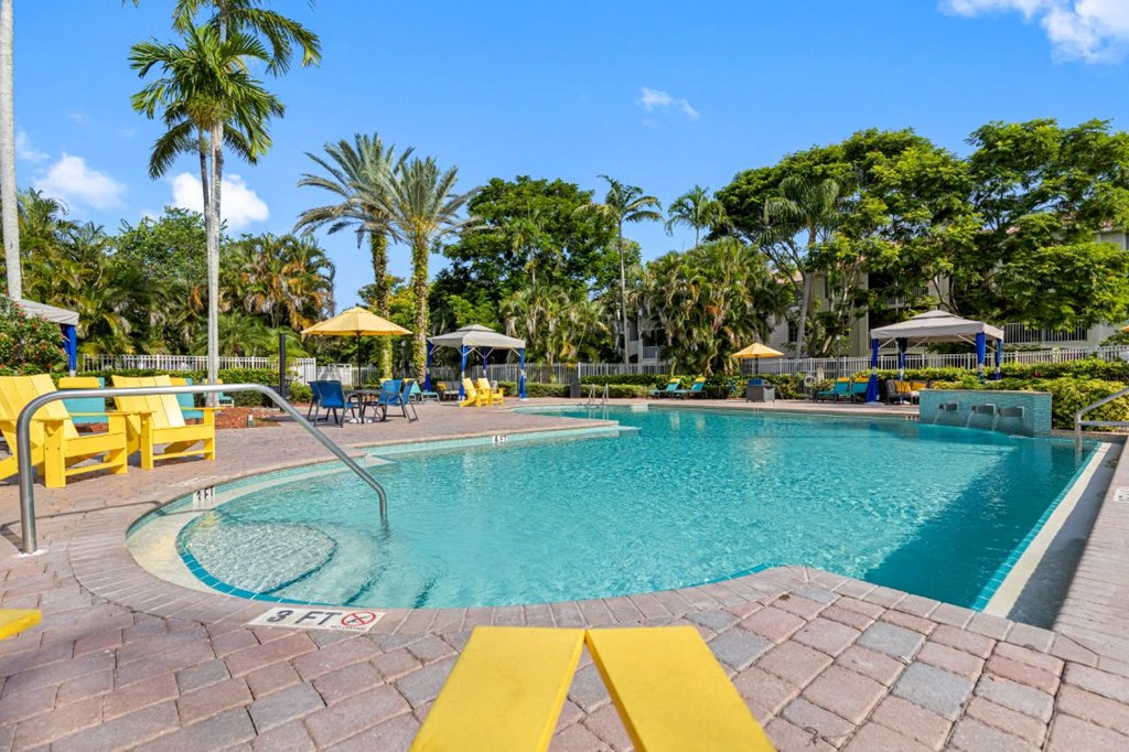 A large outdoor swimming pool surrounded by palm trees and lounge chairs.