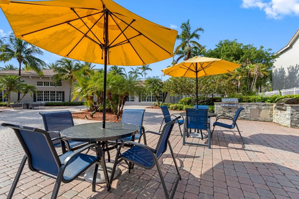 A yellow umbrella shades a table with blue chairs.