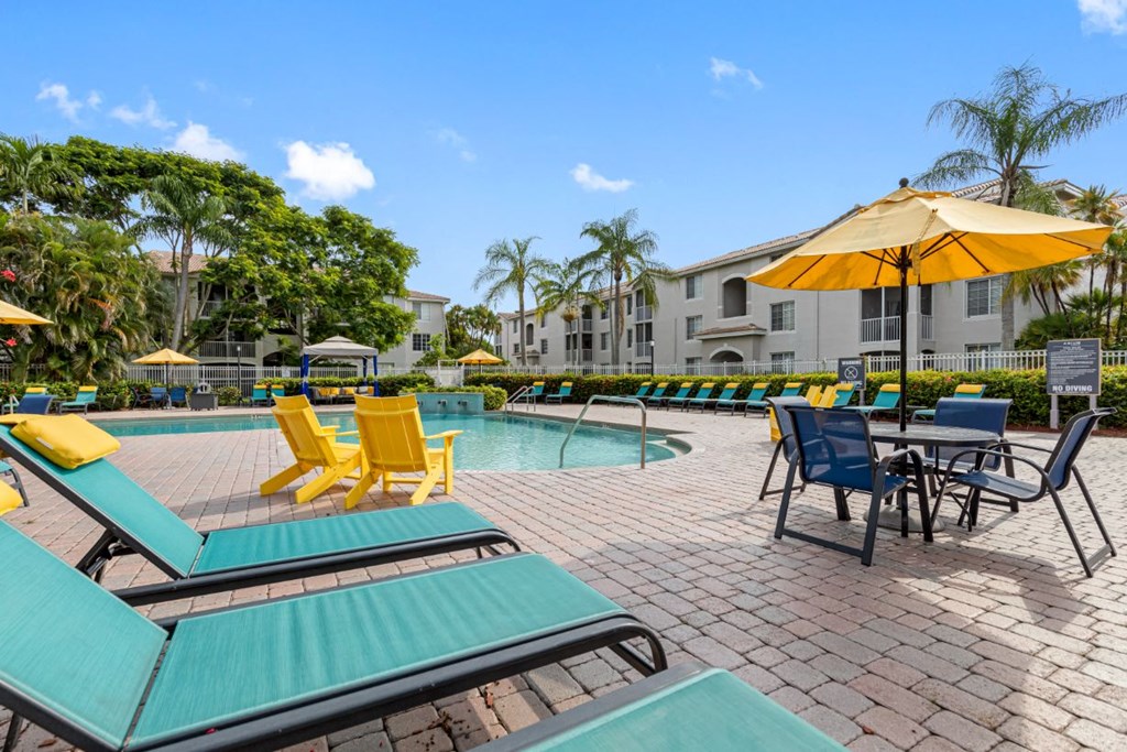 A sunny day at the pool with yellow and blue lounge chairs and umbrellas.