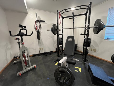 A home gym with a weight bench, barbell, dumbbells, and a stationary bike.