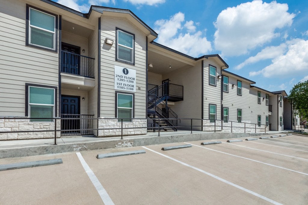 The image shows a multi-story building with a parking lot in front of it.