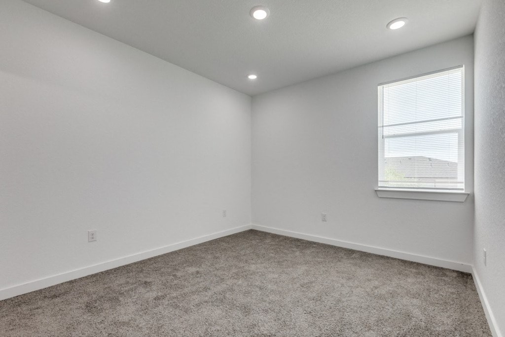 A room with a carpeted floor and a window with blinds.