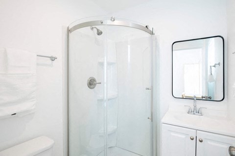 A white bathroom with a glass shower door and a white sink.