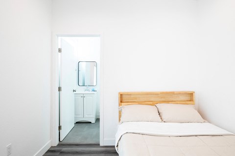 A white bedroom with a bed and a mirror.