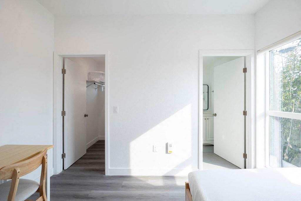 A white bedroom with a bed, table and a window.