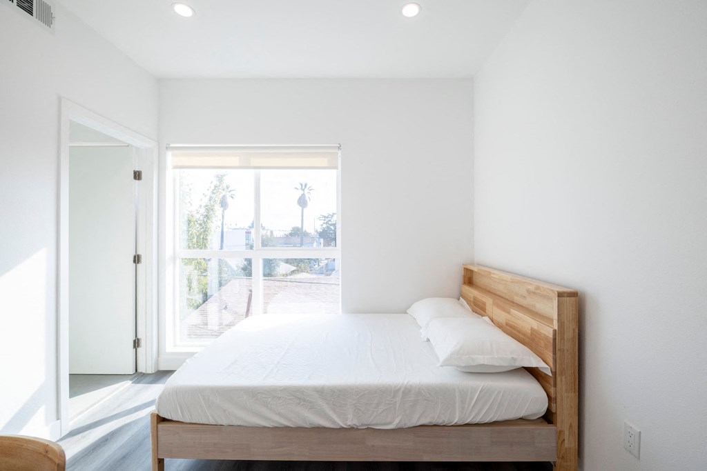 A bed with a wooden headboard and white pillow is in a room with white walls.