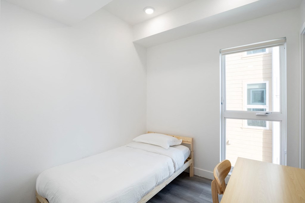 A bedroom with a bed, table and chair.