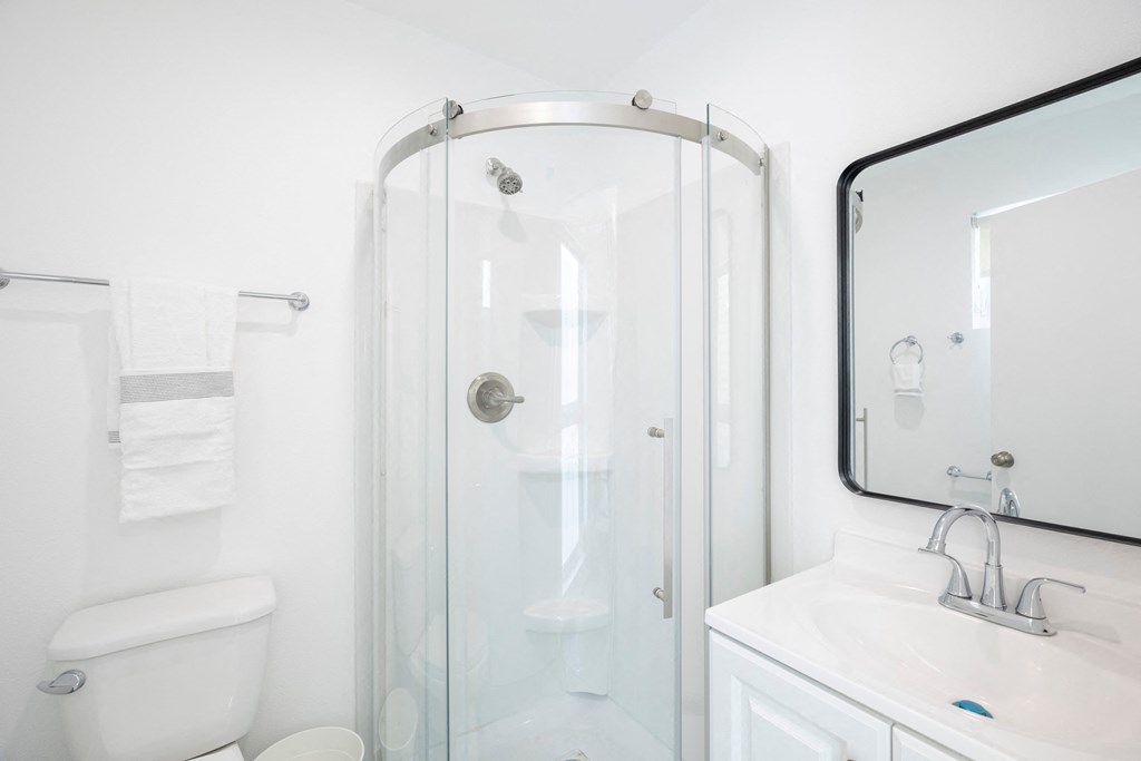 A white bathroom with a glass shower door and a white toilet.