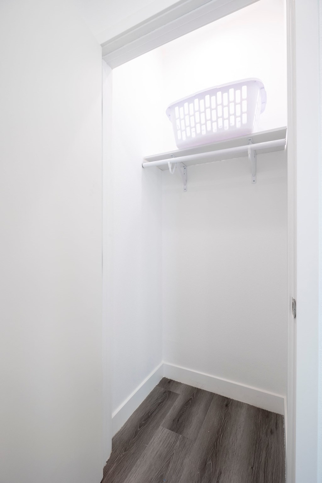 A white laundry basket is on a white shelf in a white room.