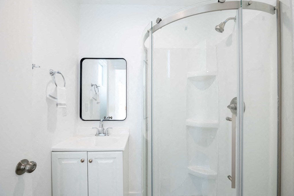 A white bathroom with a sink, mirror, and shower.
