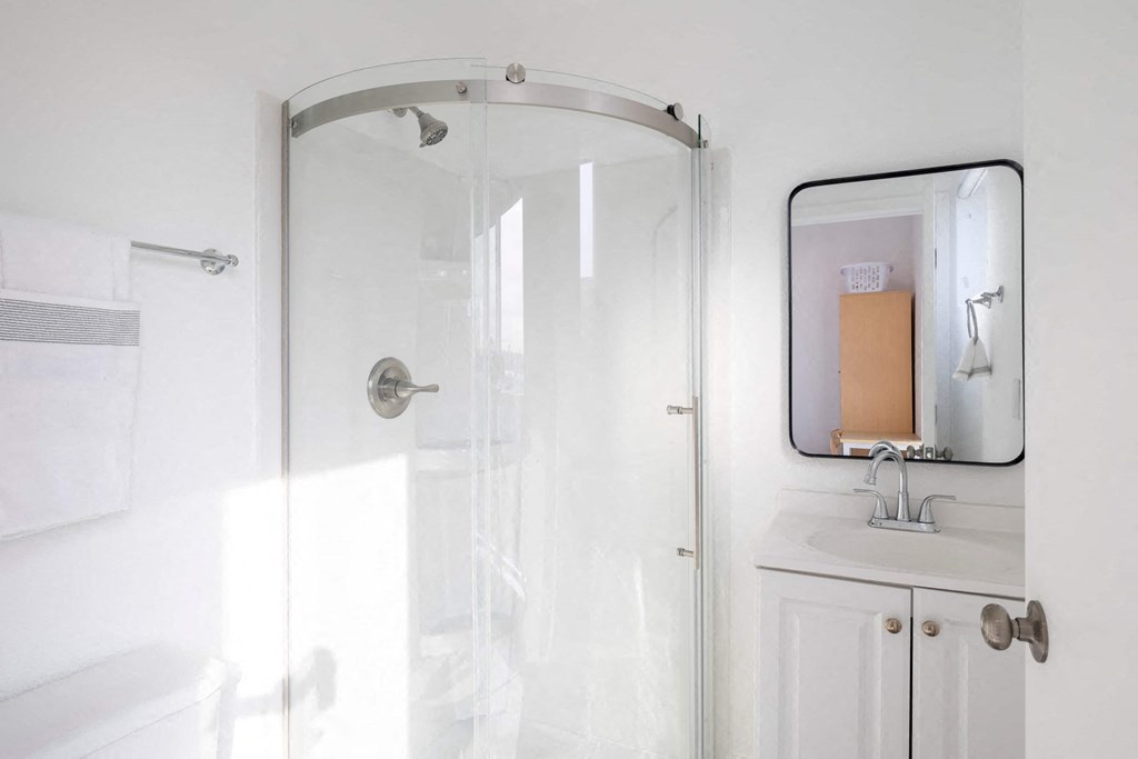 A white bathroom with a glass shower door and a mirror above a sink.