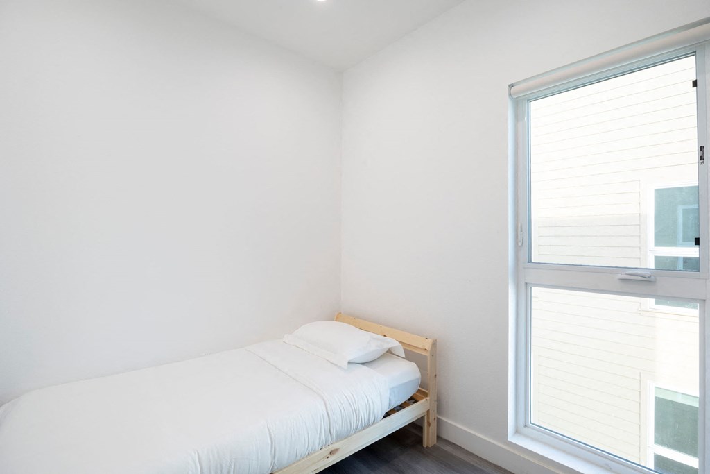 A white bed with a white pillow sits in a room with a window.