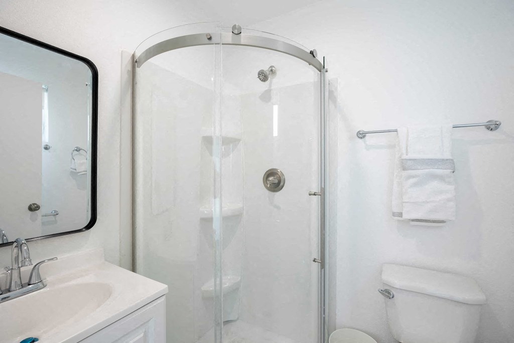 A white bathroom with a sink, toilet, and shower.