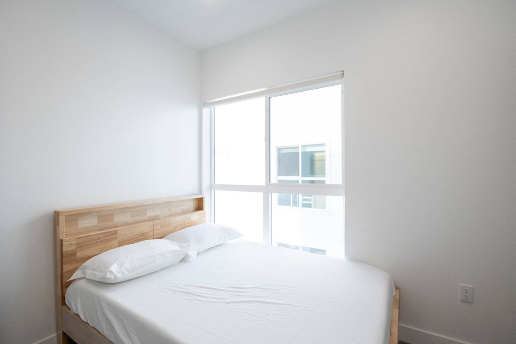 A white bed with a wooden headboard and two pillows in a room with a window.