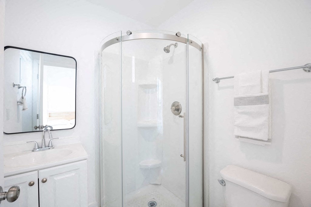 A white bathroom with a glass shower door and a white toilet.