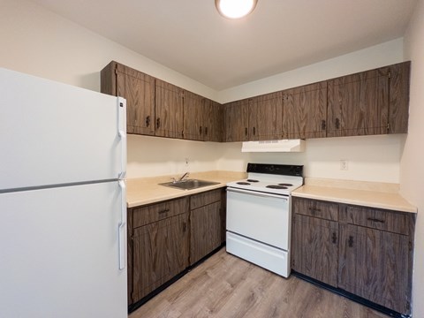 A kitchen with a white refrigerator, white stove, and wooden cabinets.