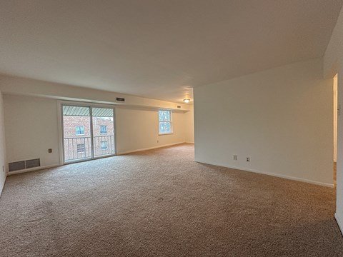 A large, empty room with carpeted flooring and a window with a view of a building outside.