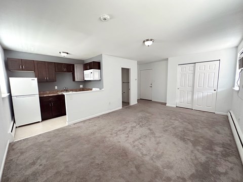 A spacious room with a kitchen area and a carpeted floor.