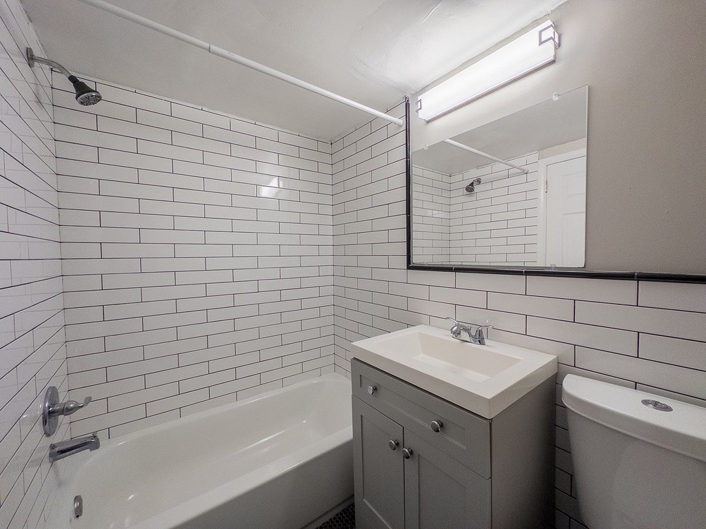A white tiled bathroom with a sink, mirror, and bathtub.