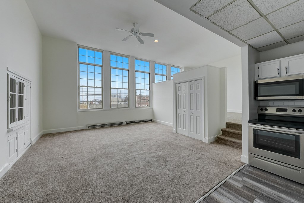 A spacious living room with a grey carpet and a ceiling fan.