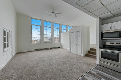 A spacious living room with a grey carpet and a ceiling fan.