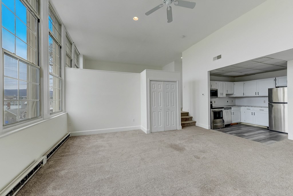 A spacious living room with a carpeted floor and a ceiling fan.