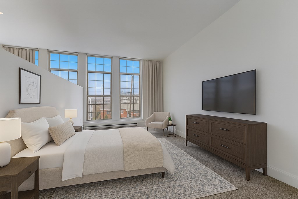 A room with a carpeted floor, a ceiling fan, and a view of a cityscape through large windows.