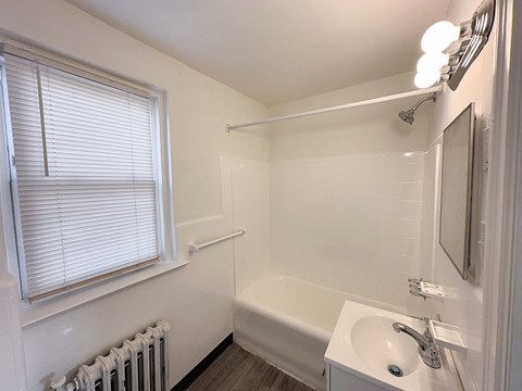 A white bathroom with a tub, sink, and window.