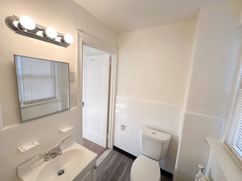 A white toilet is in a bathroom with a sink and mirror.