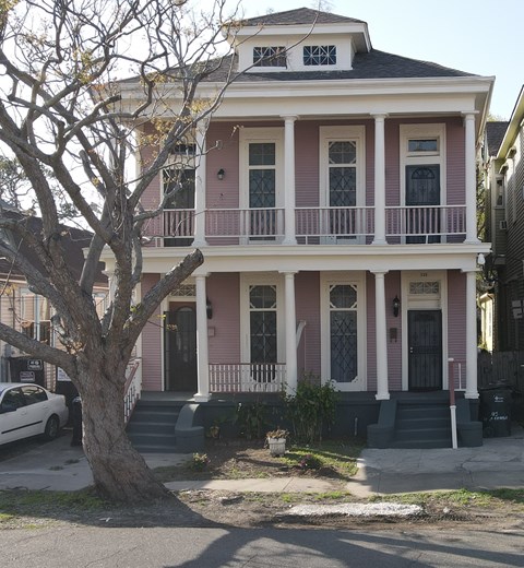 A two-story house with a balcony and a tree in front.