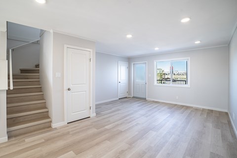 A spacious room with light wood flooring and white walls.