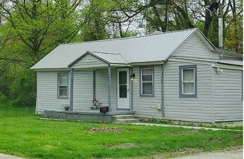 A small house with a grey siding and a white door.