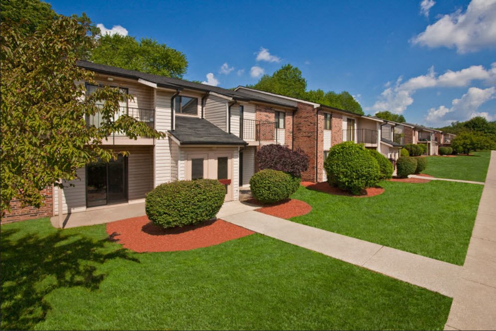 A row of houses with green lawns and trees in front.