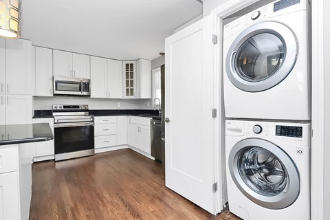 A white washing machine is in a white cabinet in a white kitchen.
