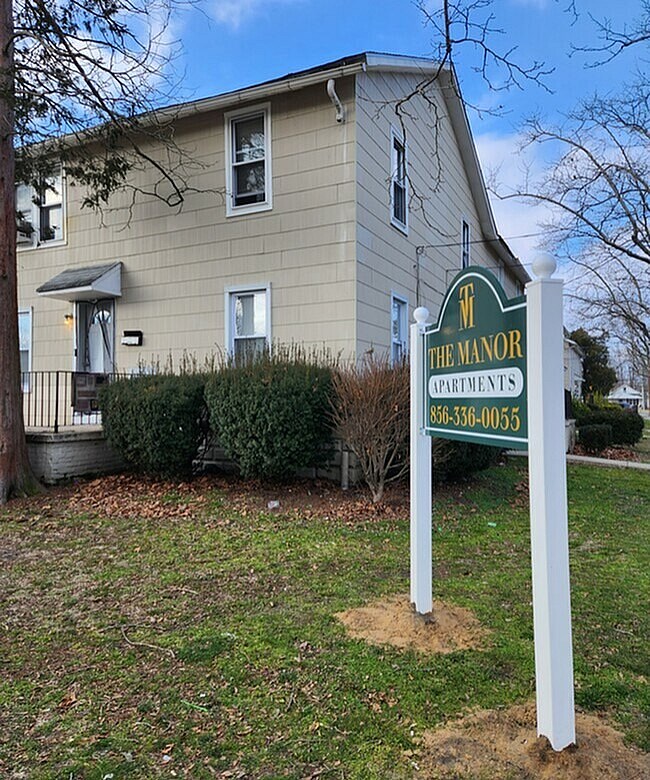 A sign for The Manor Apartments stands in front of a building.