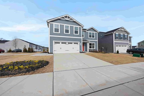 A grey house with a red door is in front of a row of houses.